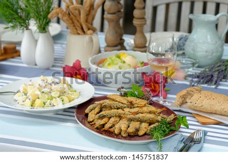 Fried sardines with potato salad, bread and a glass of white wine on the table. Typical Italian summer lunch/dinner setting