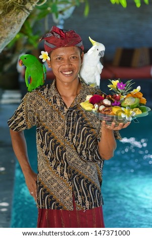 Asian waiter with a tray of tropical fruits in an exotic setting. Shoot in a luxury resort on Bali island, Indonesia