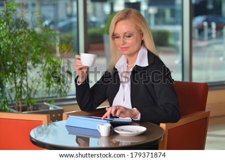 Candid photo of a attractive middle-aged blond businesswoman working at hotel lobby with a tablet pc and drinking coffee