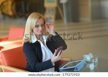 Candid photo of a attractive middle-aged blond businesswoman working at hotel lobby with a tablet pc/smartphone and drinking coffe