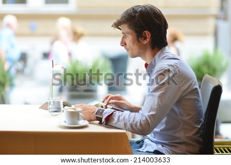 Young fashion man / hipster drinking espresso coffee in the city cafe during lunch time and working on tablet computer