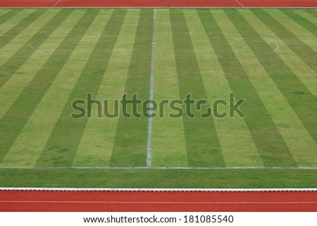 A realistic textured grass football , green natural grass of a soccer field with red running track and white line.
