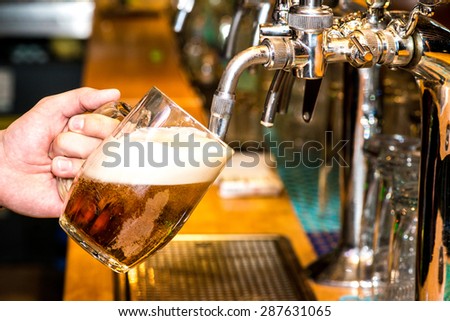 Close-up of bartender hand at beer tap pouring a draught lager beer