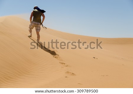 Sahara desert landscape with blue sky. Dunes background with man from behind walking