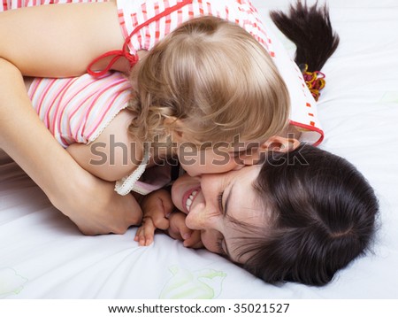 Little girl biting her mom while playing on a bed