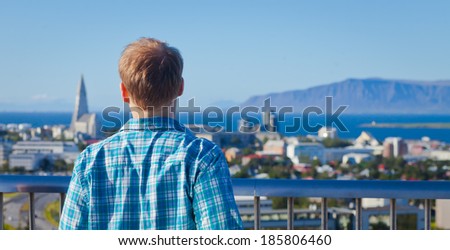 A tourist with Beautiful super wide-angle aerial view of Reykjavik, Iceland with harbor and skyline mountains and scenery beyond the city, seen from the observation tower of Hallgrimskirkja Cathedral.