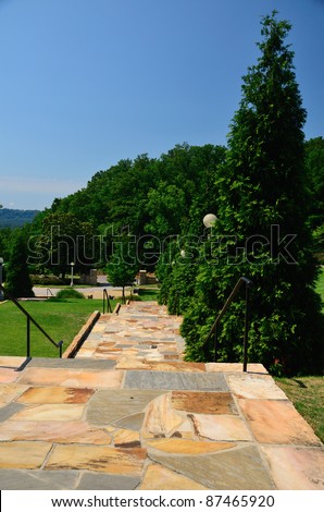 Flagstone walkway lined with trees leads into the park.