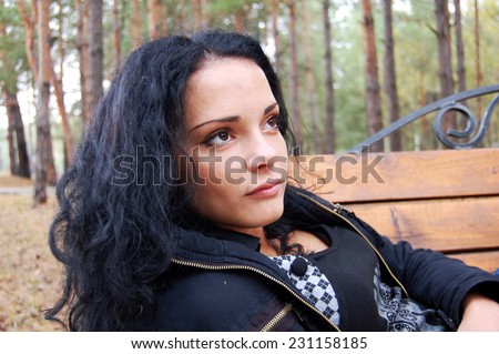 beautiful young woman in autumn park. Sad brunette sitting on a bench