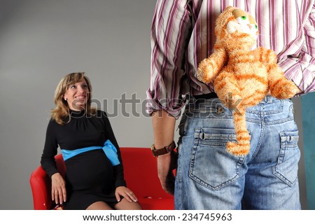 man hides behind a toy. a man gives her a toy. girl sitting on the couch waiting for a gift