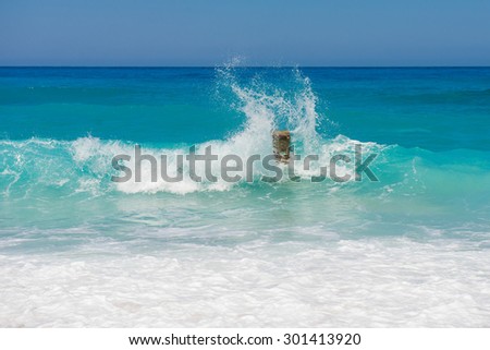 Waves crashing on rocks. blue waves, sand beach and blue sky. Greece, the island of Lefkada, Yialos Beach, Gialos. one rock in the waves