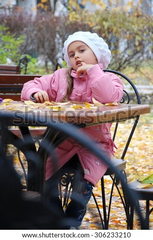 sad girl in the autumn. little girl sitting alone at a table cafe. girl in a pink coat was left alone. No family, no parents. Girl waiting for mum and dad. without family