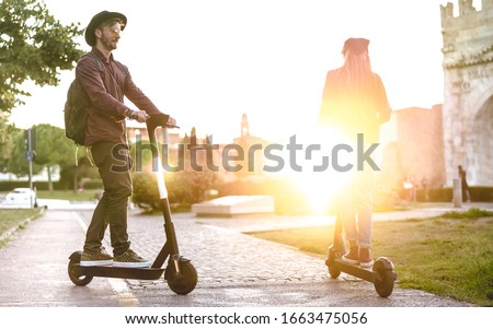 Modern couple using electric scooter in city park - Milenial students riding new ecological mean of transport - Green eco energy concept with zero emission - Bright warm filter with sunshine halo