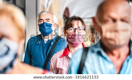 Crowd of adult citizens walking on city street - New reality lifestyle concept with senior people with covered faces - Selective focus on bearded man with blue protective mask