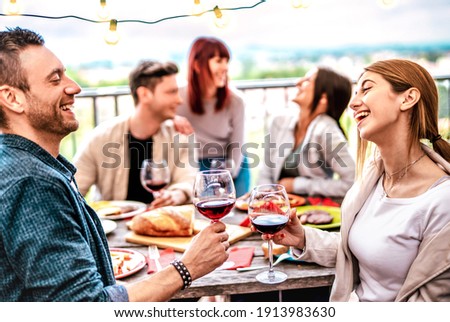 Happy people having fun drinking wine on terrace at private dinner party - Young friends eating barbeque food at restaurant together - Dinning lifestyle concept on warm filter - Focus on right glass