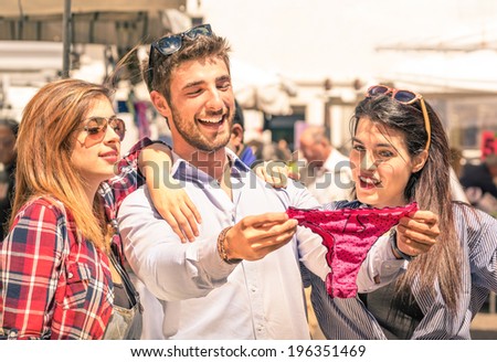Group of happy young people at the weekly cloth market looking at female underwear - Best friends sharing free time having fun and shopping in the old town in a sunny day