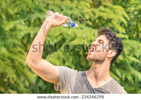 Sporty man refreshing with cold water after run training work out in the park - Sport fitness young happy model taking a break after jogging in the nature