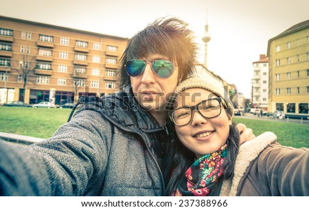 Hipster couple of tourists taking a selfie in Berlin City - Multiracial concept of friendship and fun with new trends and technology - Asian girl with alternative young fashion handsome guy