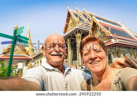 Senior happy couple taking a selfie at Grand Palace temples in Bangkok - Thailand adventure travel to asian destinations - Concept of active elderly and fun around the world with new technologies