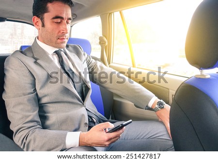 Young handsome businessman sitting in taxi cab while texting sms with smartphone - Business concept with modern man using smart phone - Soft vintage editing with artificial sunlight from the window