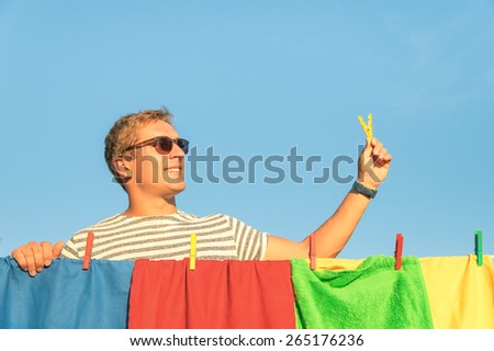 Young handsome hipster man hanging colorful laundry with clothespin - Concept of single lifestyle taking care on houseworks - Funny guy hanging multicolored clothes on bright sunny day outdoors