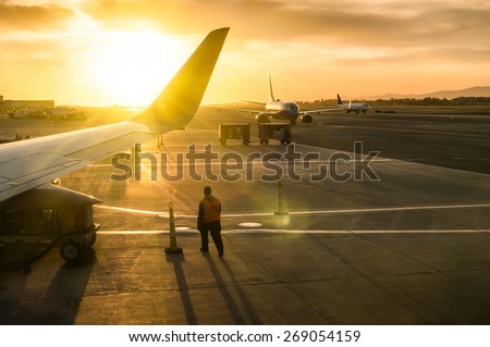 Generic working man walking near airplane wing at terminal gate of international airport at sunset - Concept of emotional travel around the world - Soft focus and sun lens flare due to backlighting