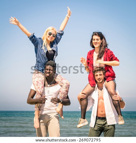 Multiracial best friends at beach having fun with piggyback game - Spring summer concept of multi ethnic friendship against racism - Young people playing together outdoors - Soft focus on action scene