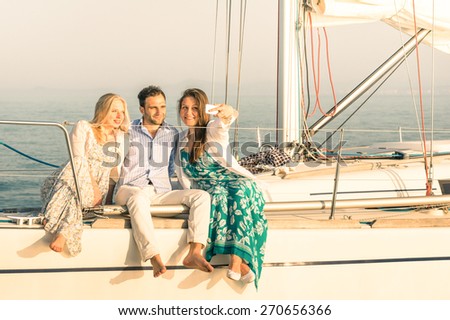 Young people taking selfie on exclusive luxury sailing boat - Concept of friendship and travel with best friends using modern smartphone as new trends and technology - Warm sunset color tones