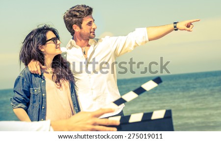 Couple in love acting for romantic movie at beach - Cinema industry concept with ciak slate - Confident guy and happy girlfriend modern lifestyle - Focus on male face and soft vintage filtered look