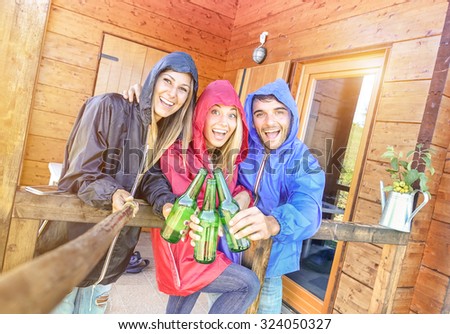 Best friends taking tilted selfie at camping bungalow with sunshine after the rain - Youth and freedom concept outdoors in autumn vacations - Young people having fun and cheering with bottled beer
