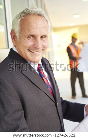 happy confident business man with construction workers in the background holding building blueprints