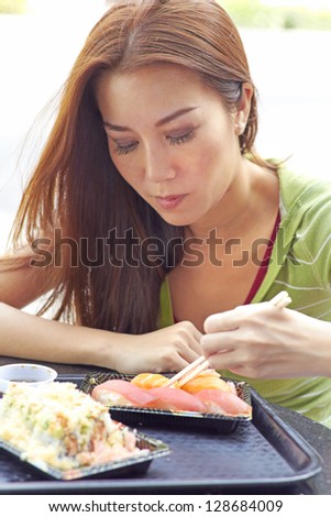 Young casual Asian woman eating sushi with chopsticks. Vertical Shot.