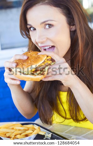 Portrait of beautiful young female eating fresh burger. Vertical Shot.