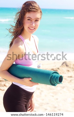 Beautiful young white female holding yoga mat at the beach