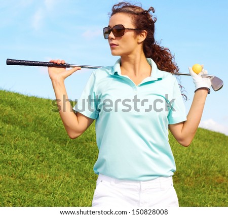 pretty female golfer relaxing holding ball and golf club against clear blue sky.