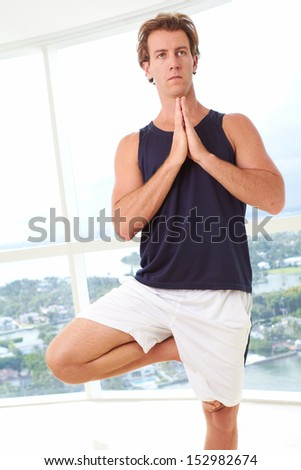 Caucasian male doing yoga tree pose indoors in high  rise apartment