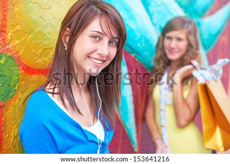Portrait of young female listening music while friend standing in background with a shopping bag. Horizontal shot.