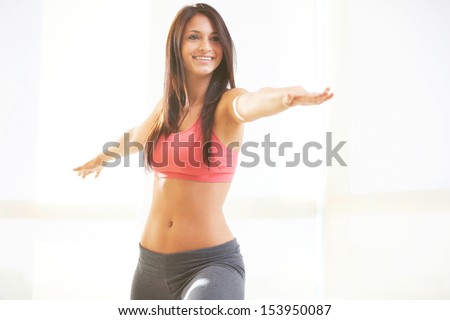 Young beautiful female doing yoga warrior pose in sky rise gym with copy space.
