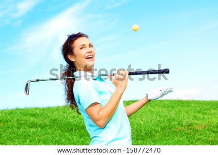 beautiful playful female golfer relaxing throwing ball in the air laughing and holding golf club against clear blue sky.