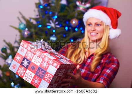 Christmas woman giving. Pretty blonde female giving present on Christmas Morning. Beautiful young blonde girl holding Christmas present with copy space.Shallow depth-of-field.