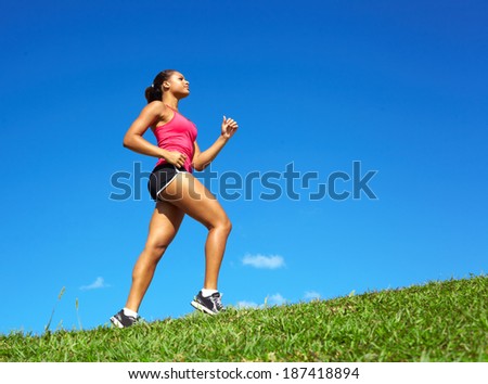 Sporty mixed race woman jogging. Color image, copy space, african american ethnicity female running with green grass and blue sky.