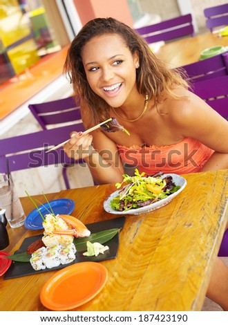 Pretty Mixed Race Woman Enjoying A Meal At A Restaurant. African American female enjoying japanese cuisine at a fancy restaurant, using chopstick and really happy.