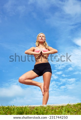 Low angle view of beautiful young woman practicing tree yoga pose against sky