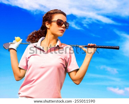 Low angle view of confident woman holding golf club on shoulders against blue sky