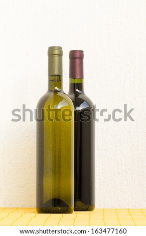 White and red wine bottles on a yellow mat in front of a white wall in natural light