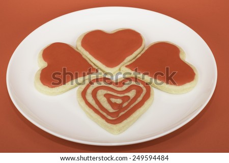 Four homemade valentine sugar cookies with red icing on a white plate against a red background