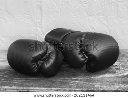 Pair of black boxing gloves on an old wood grained table against a textured wall in black and white