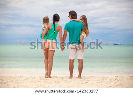 Back view of beautiful family with two daughters at exotic beach on sunny day