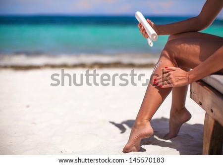 young woman apply cream on her smooth tanned legs on tropical beac