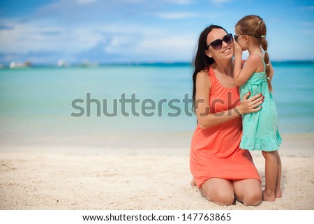Young mother and her cute little girl whispering on the white beach