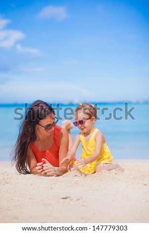 Young mother and her little daughter lying on white sand beach